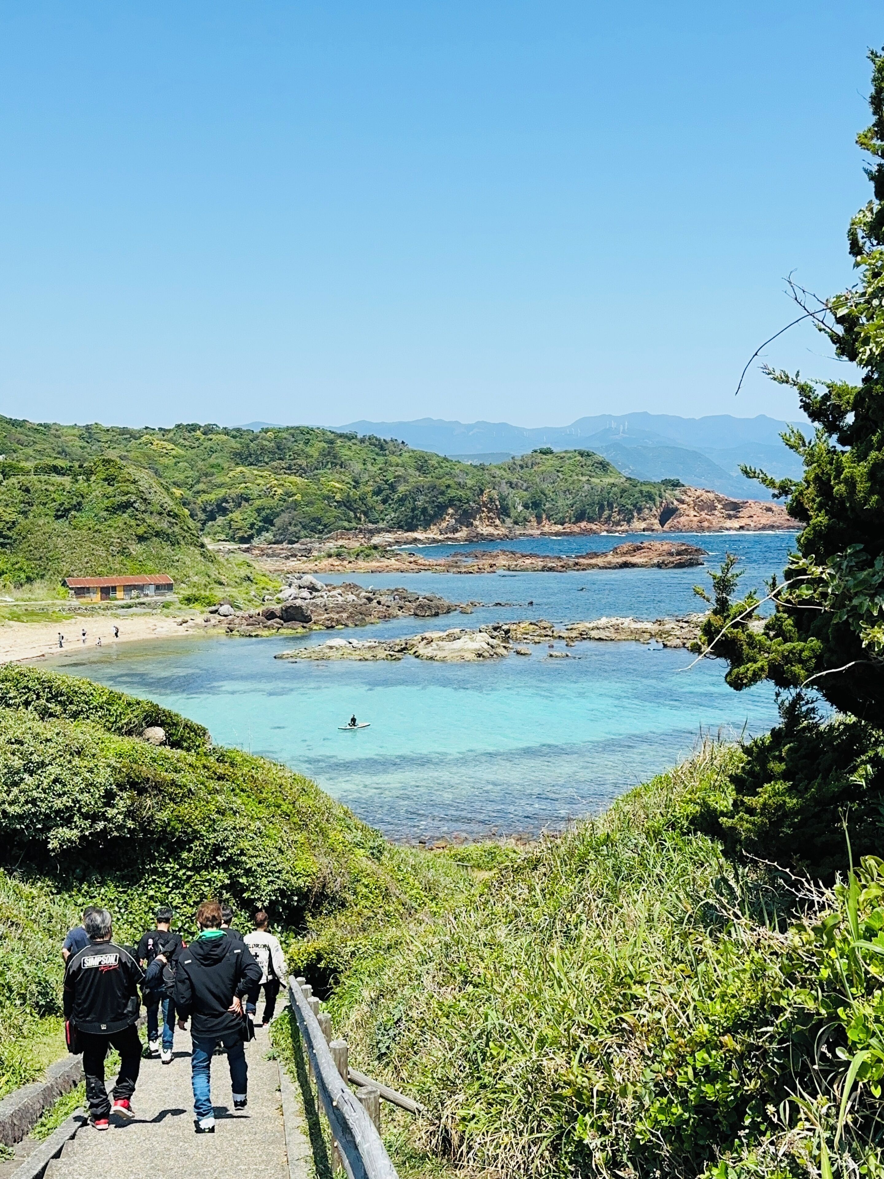 A coastal area with a clear view of the sea, rocky formations, and a path leading to a beach.