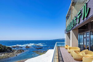 A coastal hotel with a balcony overlooking the sea, featuring wicker chairs and a clear view of the ocean.