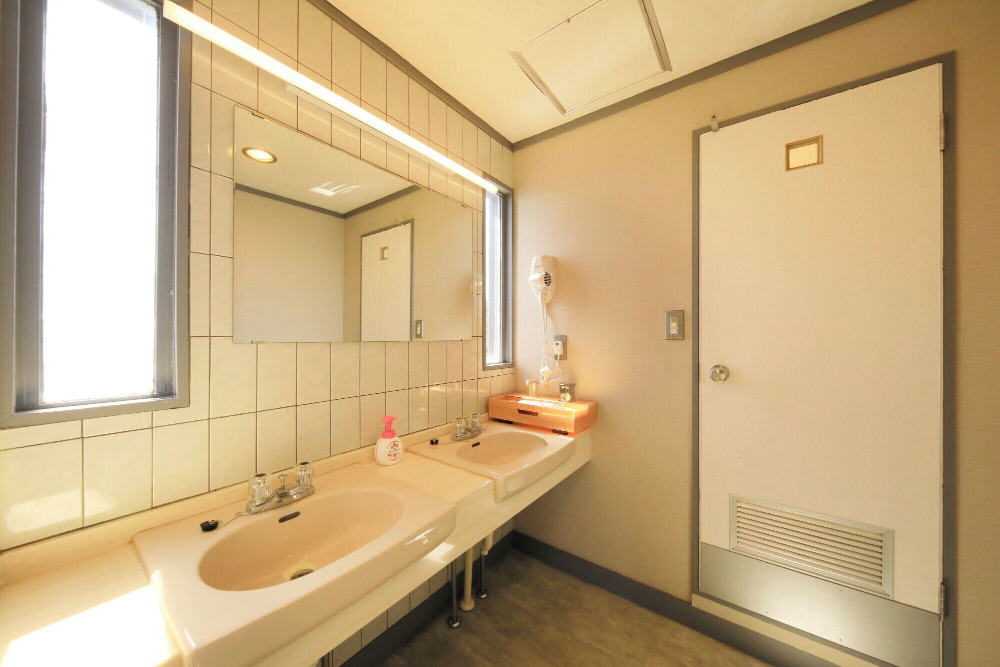 A bathroom with two sinks, a mirror, a hairdryer, and a door.