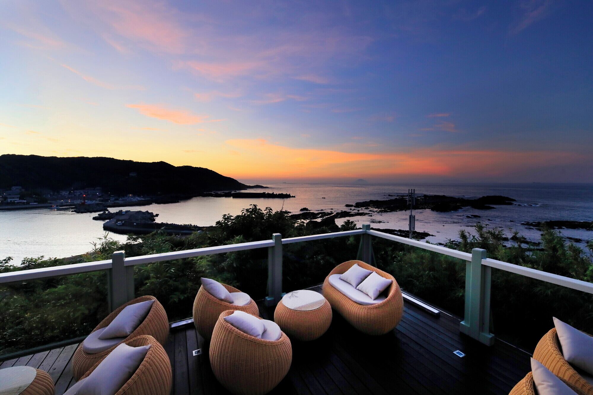 A deck with wicker chairs and a view of the sea at sunset.