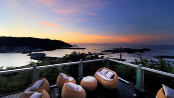 A deck with wicker chairs and a view of the sea at sunset.