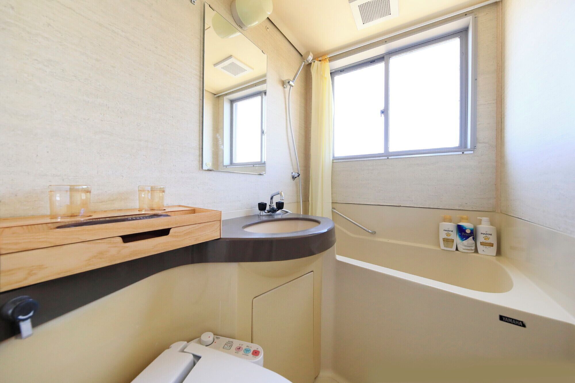Ein kleines Badezimmer mit Waschbecken, Spiegel und Toilette. An der Wand befinden sich zwei Flaschen Pantene Shampoo und Conditioner.