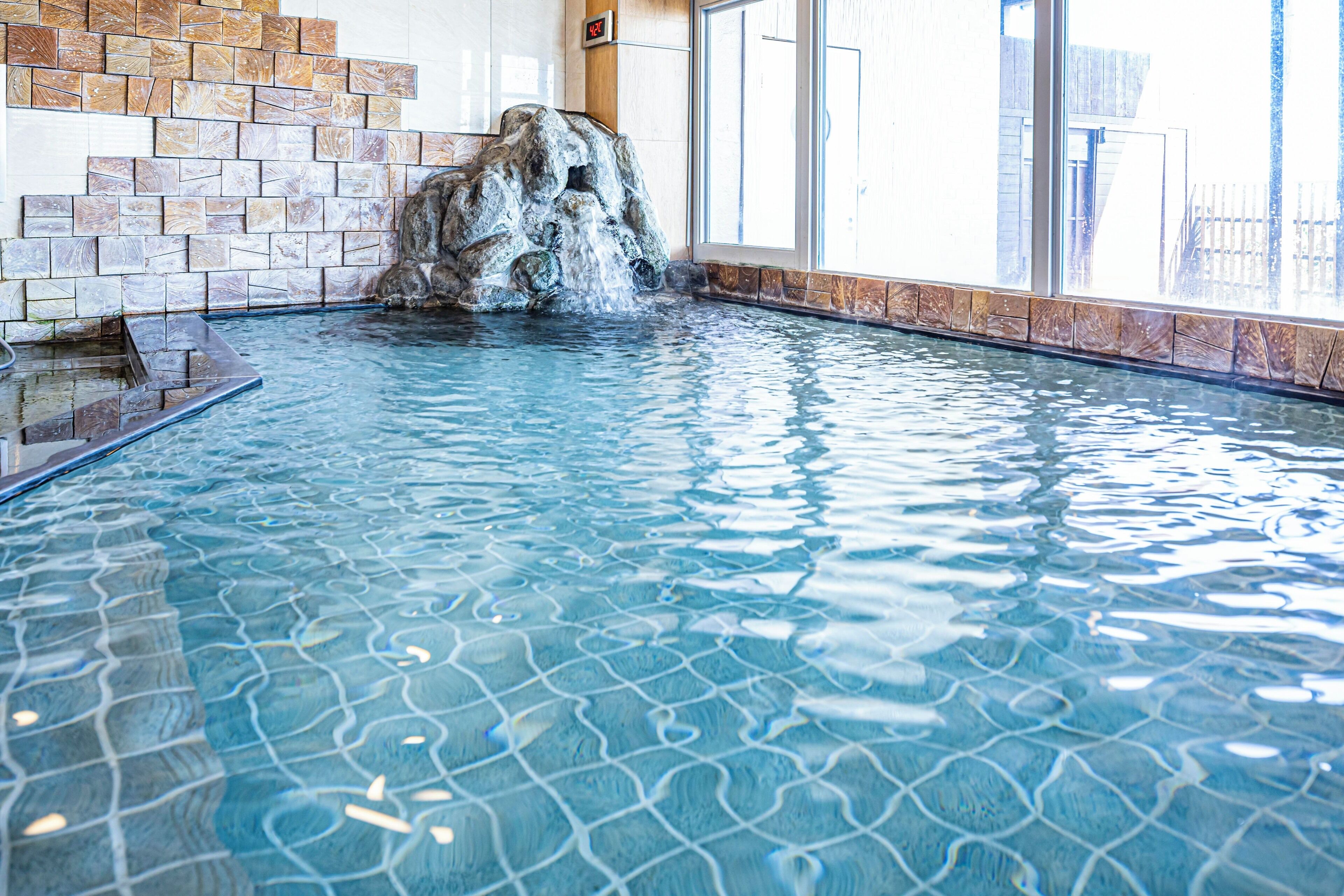 An indoor swimming pool with a waterfall feature and tiled walls.
