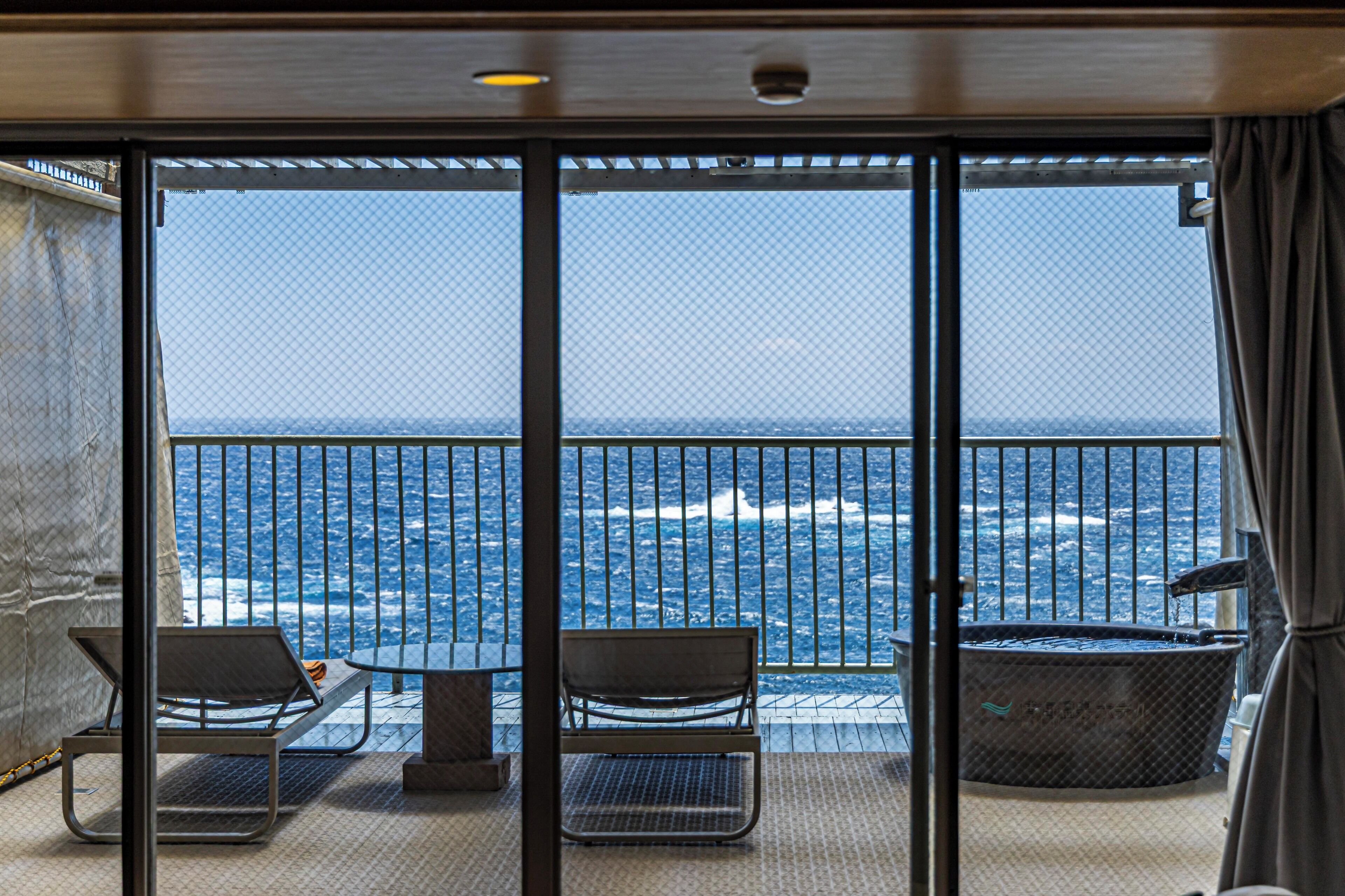 A balcony with two chairs and a hot tub overlooking the ocean.