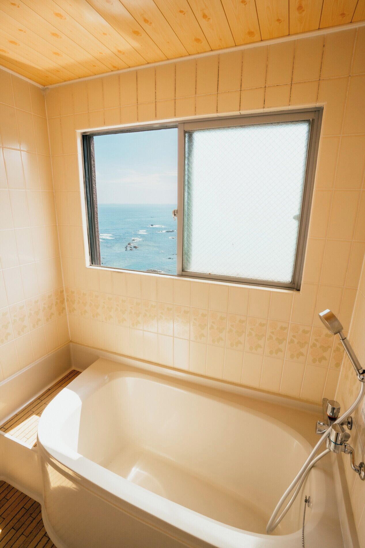 A bathroom with a bathtub, a window with a view of the sea, and tiled walls.