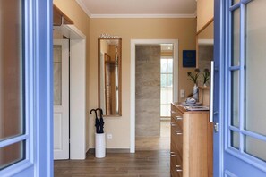 A hallway with a 'Welcome' sign, a white trash bin, a wooden cabinet with a vase, and a door leading to another room.
