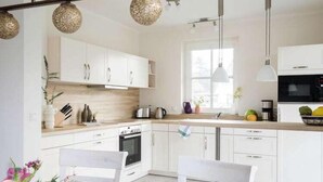 Una cocina moderna con armarios blancos, encimera de madera y horno empotrado. Hay luces colgantes y un ventanal que proporciona luz natural.