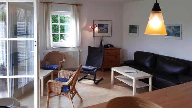 Een gezellige woonkamer met een zwarte leren bank, rieten fauteuils, een houten tafel en een vloerlamp.