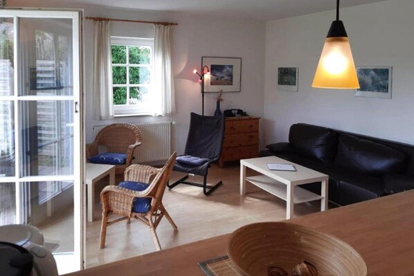 A cozy living room with a black leather sofa, wicker chairs, a wooden table, and a floor lamp. - Ferienwohnungen Blaues Haus, Putbus (Putbus)