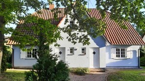 Een wit huis met een pannendak, een pad van baksteen dat naar de ingang leidt, en een kleine tuin.