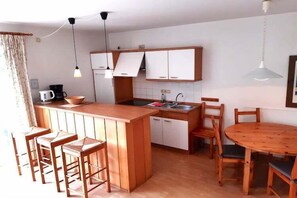 Une cuisine compacte dotée d’un îlot central, de tabourets de bar, d’une table à manger et de luminaires suspendus.