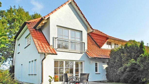 Une maison à deux étages avec un toit recouvert de tuiles rouges, un balcon et un patio aménagé avec du mobilier d’extérieur.
