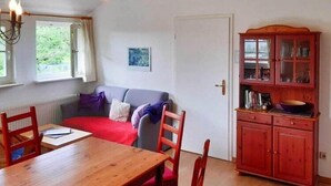Une pièce comprenant une table à manger en bois, des chaises rouges, un canapé rouge, un meuble en bois et une fenêtre avec des rideaux.
