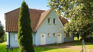 Une maison bleu clair avec un toit en tuiles, une pelouse bien entretenue et un grand arbre à feuilles persistantes au premier plan.