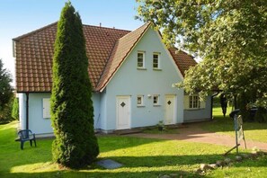 A light blue house with a tiled roof, a well-maintained lawn, and a tall coniferous tree in the foreground.
