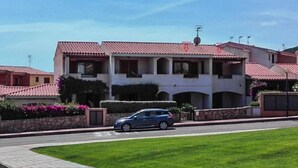 A two-story building with a red-tiled roof, a car parked in front, and a well-maintained lawn. - Apartment in Cannigione (Cannigione)
