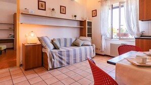 A compact room with a bed, a table with a cup, a chair, a shelf with items, and a window with curtains. - Residence Casa & Vela with private beach, Oggebbio (Oggebbio)