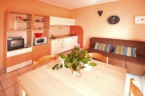Un espace de vie compact comprenant un coin cuisine, une table à manger, un canapé et une horloge murale.