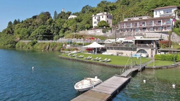 A lakeside dock with a boat, a grassy area with lounge chairs, and buildings on a hillside. - Residence Casa & Vela with private beach, Oggebbio (Oggebbio)