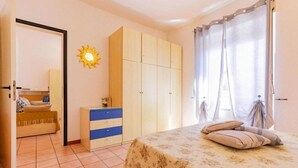 A bedroom with a bed, a wardrobe, a dresser, a sun-shaped wall decoration, and a window with curtains. - Residence Casa & Vela with private beach, Oggebbio (Oggebbio)