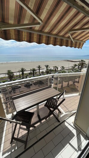 Un balcón con vista a la playa, una mesa y sillas.