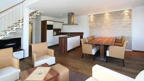 A modern living room with a wooden dining table, beige sofas, a TV, and a kitchen in the background. - Wohnung in Cuxhaven. (Cuxhaven)
