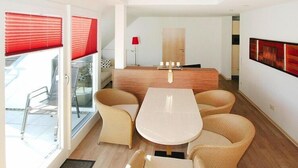 A modern interior with a dining area featuring a white table and wicker chairs, a wooden counter, and a red lamp. - Wohnung in Cuxhaven. (Cuxhaven)