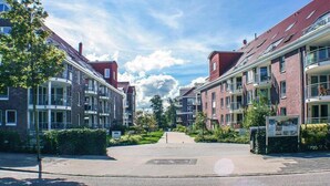 A residential street with brick apartment buildings, a clear sky, and a well-maintained green area in the center. - Wohnung in Cuxhaven. (Cuxhaven)