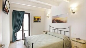 Une chambre à coucher comprenant un lit, des tables de chevet, une commode, une fenêtre avec des rideaux et des œuvres d’art accrochées au mur.
