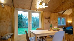 Interior de una cabaña de madera con una mesa de comedor, sillas, un sofá y vistas al exterior.