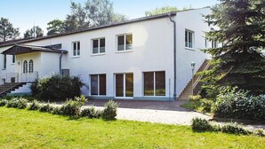 Een gebouw met twee verdiepingen, een witte gevel, een overdekte veranda en een trap die naar de bovenverdieping leidt.