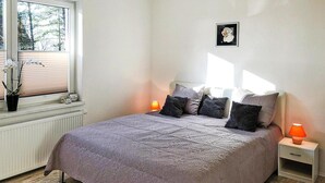Een slaapkamer met een bed, twee nachtkastjes, een raam met zonwering, een radiator en een potplant.
