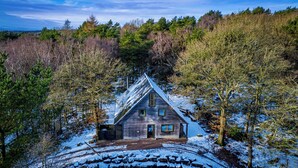 A wooden cabin surrounded by trees with a snow-covered ground.