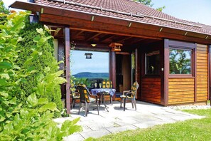 A wooden cabin with a patio, outdoor seating, and a view of the landscape.