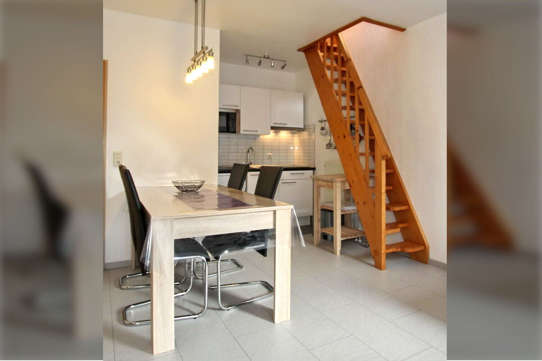 A modern kitchen with white cabinets, a wooden staircase, and a dining area with a table and chairs.