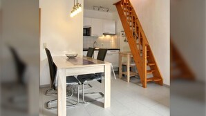 Une cuisine moderne avec des meubles blancs, un escalier en bois et un coin repas comprenant une table et des chaises.