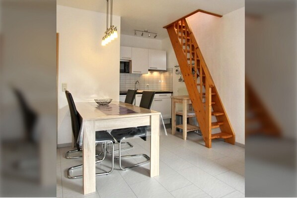 Une cuisine moderne avec des meubles blancs, un escalier en bois et un coin repas comprenant une table et des chaises.