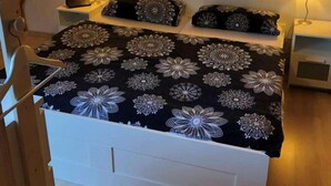 Une chambre avec un plafond en pente, un lit recouvert d’une couvre-lit à motifs floraux, deux lampes de chevet et deux tableaux encadrés accrochés au mur.