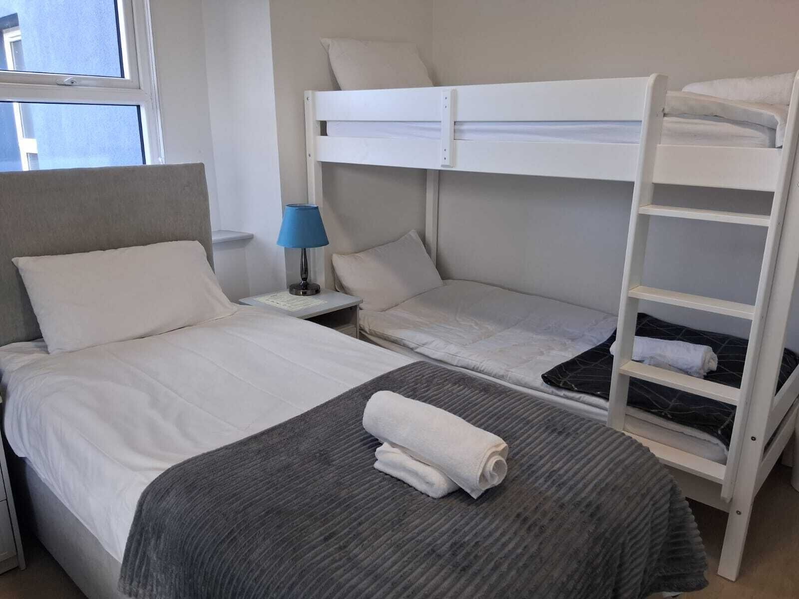 A bunk bed room with a bed, a nightstand with a lamp, and a shelf.