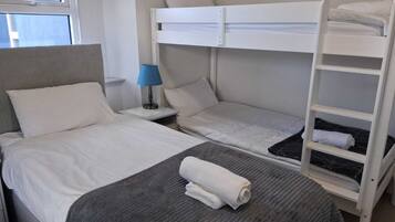 A bunk bed room with a bed, a nightstand with a lamp, and a shelf.