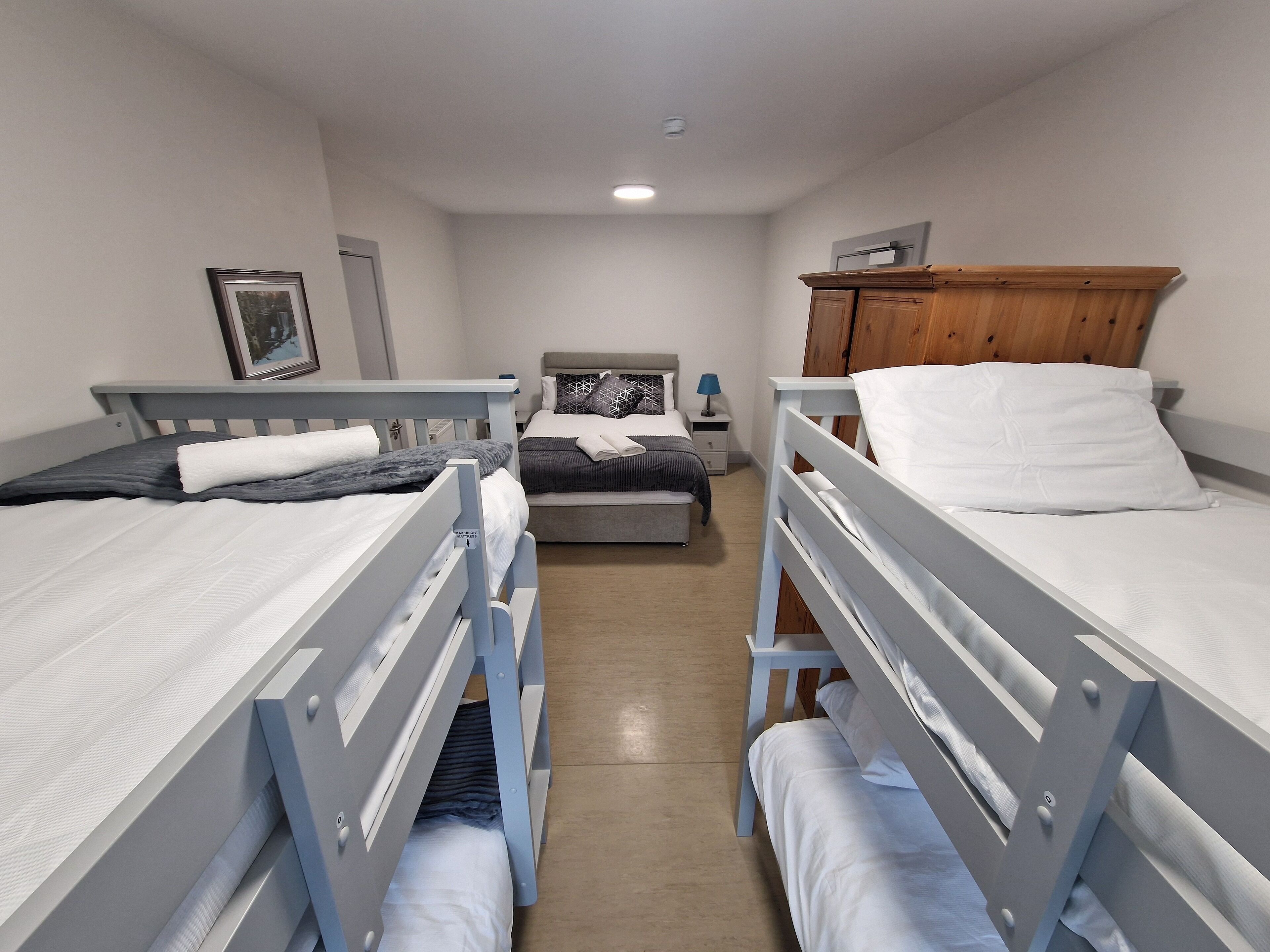 A dormitory room with bunk beds, a bedside table with a lamp, and a wooden wardrobe.