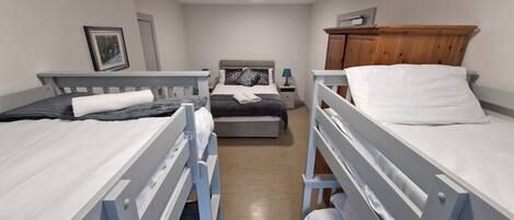A dormitory room with bunk beds, a bedside table with a lamp, and a wooden wardrobe.