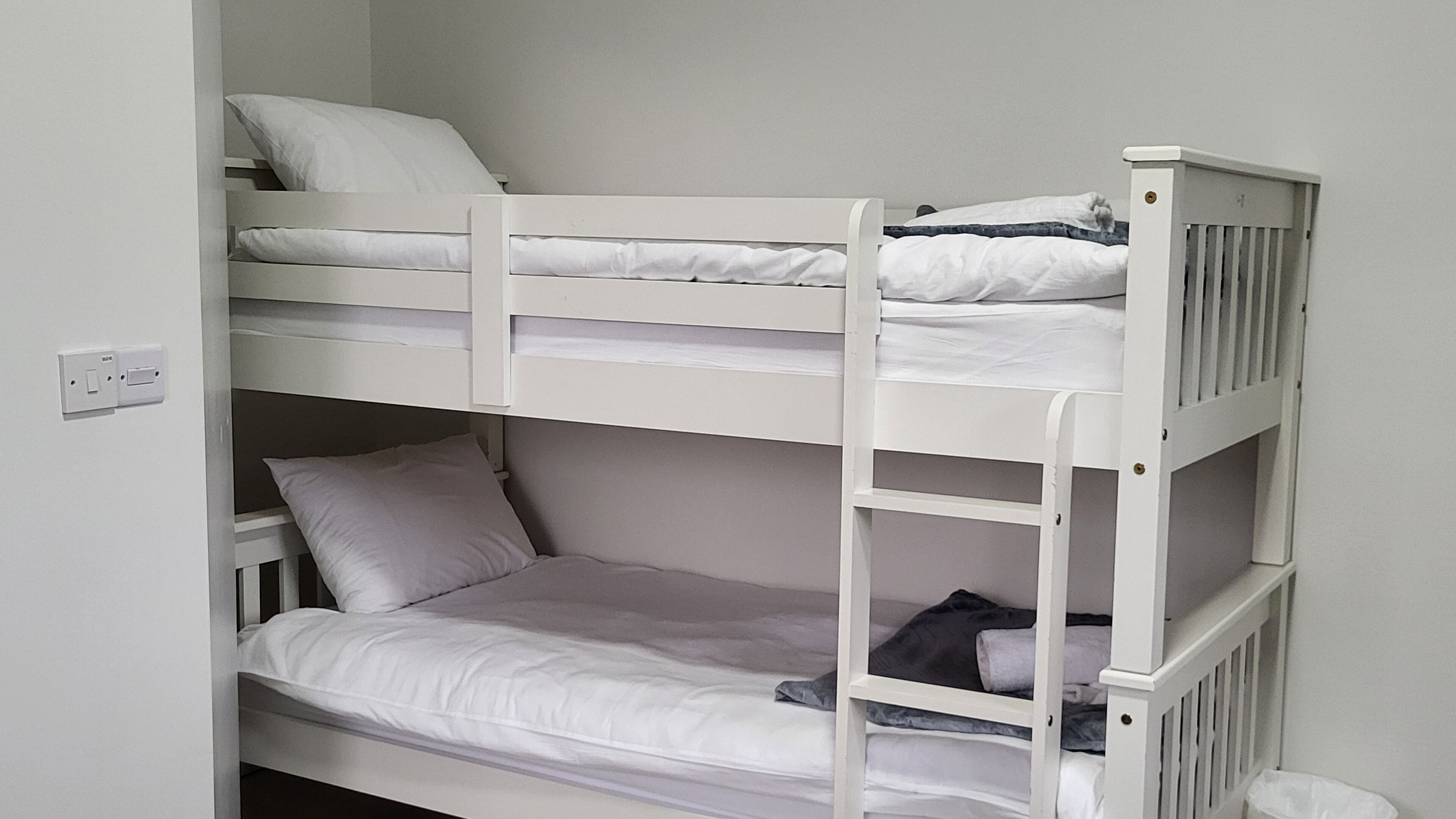 Quarto com beliches, roupa de cama branca e escada.