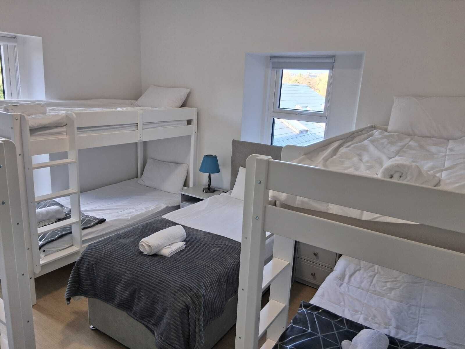 Un dormitorio con literas, una mesita con una lámpara y una ventana que da al exterior.