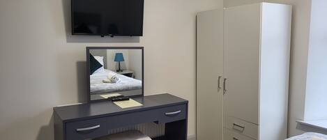 Een hotelkamer met een bed, een bureau met lades, een spiegel, een aan de muur bevestigde televisie en een kledingkast.