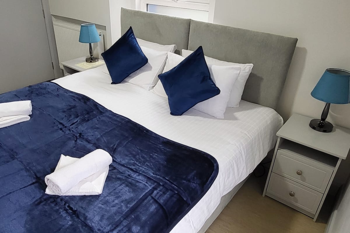 A neatly made bed with a blue bedspread, white pillows, and two blue lamps on nightstands.