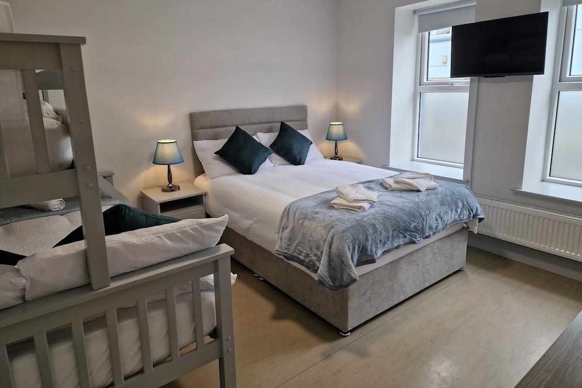 A bedroom with a bunk bed, a single bed, bedside lamps, a flat-screen TV, and a window.