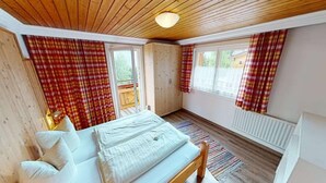 A cozy bedroom with a wooden bed, plaid curtains, and a view of a balcony. - Chalet in Wildkogel near Ski Slopes (Neukirchen)