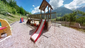 A playground with a slide and climbing structures, surrounded by a wooden fence and a bench. - Chalet in Wildkogel near Ski Slopes (Neukirchen)