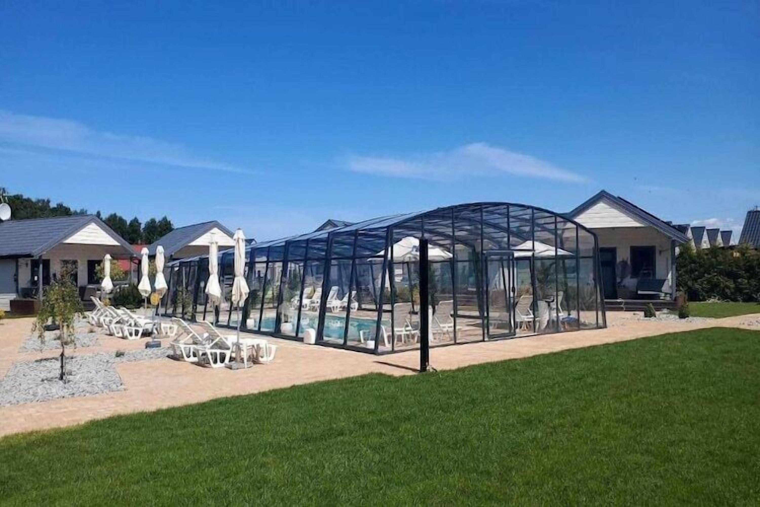 A covered outdoor area with chairs and umbrellas, a pool, and a house in the background.